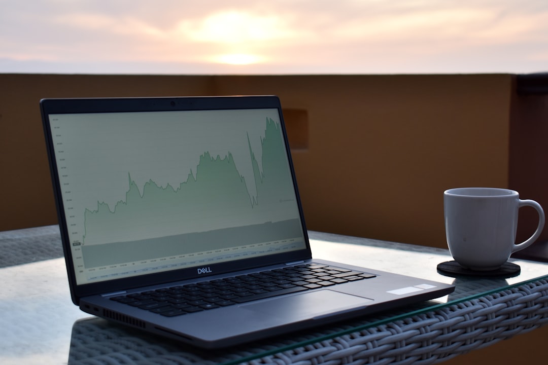 Laptop displaying a stock market graph with a cup of coffee beside it, set against a sunset backdrop.
